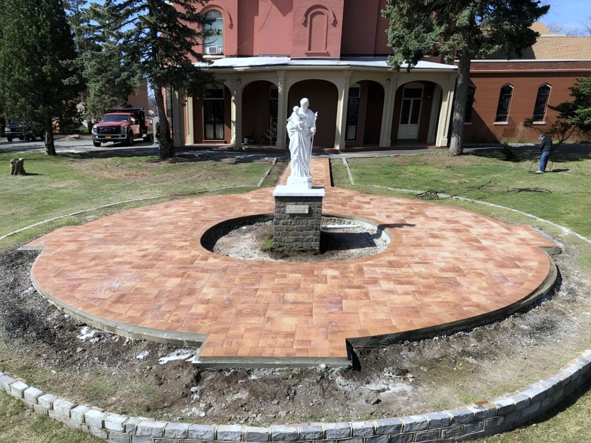 Circular brick paver patio around a statue pedestal in front of a brick building